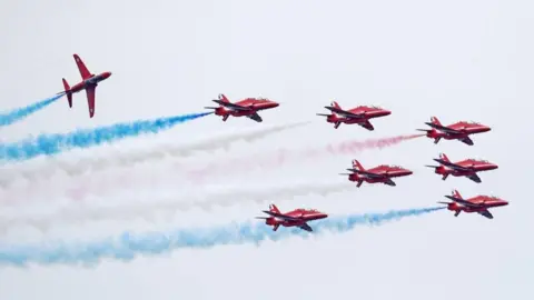 PA Media The Red Arrows at an air display. The red aircraft are trailing red, white and blue smoke