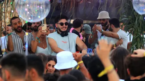 People DJ, dance and take video in a crowd at a Syrian electronic music concert