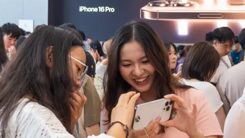 Getty Images Dua remaja putri melihat iPhone 16 Pro di Apple Store di Chengdu, Cina.