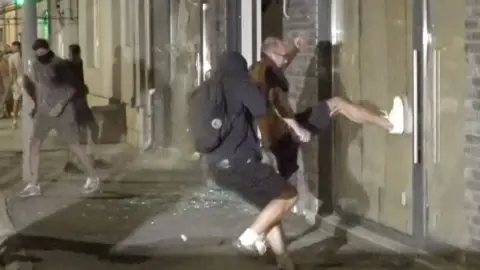 A man wearing white trainers kicks a window of an office belonging to Serbia's ruling party.