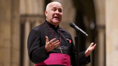 Getty Images Archbishop of York standing and holding his hands open, palms upwards, wearing his black cassock with red trim