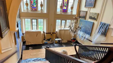 BBC News A busy interior scene of a large historic house and staircase, with sheets and plastic covering up furniture and paintings, as renovation work is being done