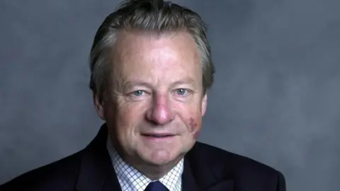 BBC Dafydd Elis-Thomas with slightly greying hair. He is wearing a black suit and is smiling and looking at the camera.