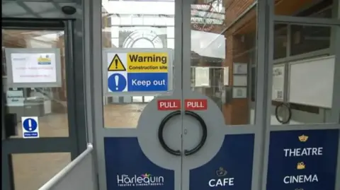 The glass front doors to Redhill's Harlequin theatre with a warning construction site sign on one of them 