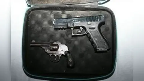 Two guns - a Glock-style pistol and a small vintage-looking enclosed-hammer revolver - lie in a small case which has black padding.