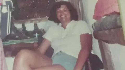 Diane Slater Lady with a brown short perm, wearing a white shirt and blue shorts