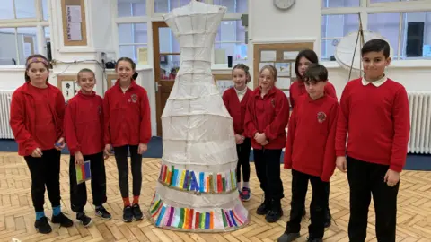 Bedminster Winter Lanterns Eight primary school pupils standing around their lantern, which has layers of coloured paper depicting books on shelves