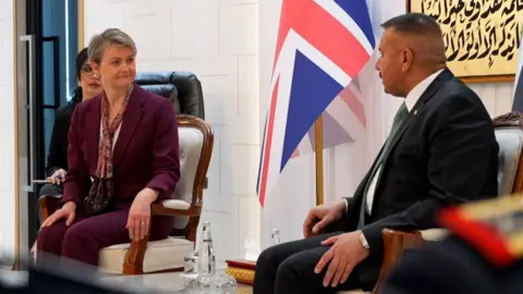 Yvette Cooper and Abdul Amir Al Shammari sitting in chairs side-by-side in front of the UK and Iraqi flags.