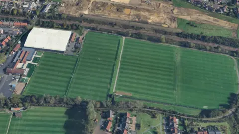 Google Aerial view of the training ground. There are five large green football pitches and a large indoor complex with a big white roof.