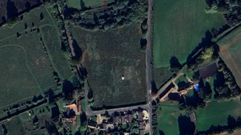 Google A satellite image of a field on the northern edge of Willows Green. The field is surrounded on three sides by roads, and there are several buildings shown at the bottom edge of the image