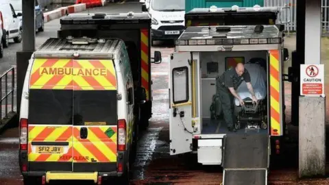 Two ambulances parked outside a hospital, one is open at the back with a man in green uniform inside