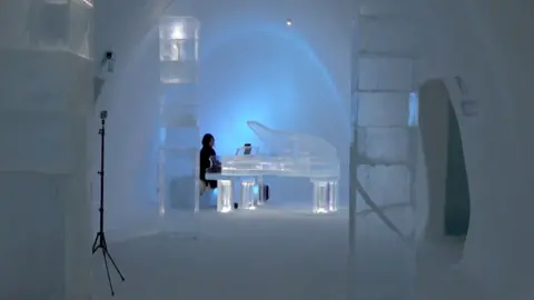 Woman plays ice piano inside ice hotel in Lapland