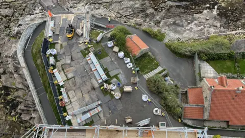 Andy Watson/BBC Aerial view of construction work on a lighthouse and island.