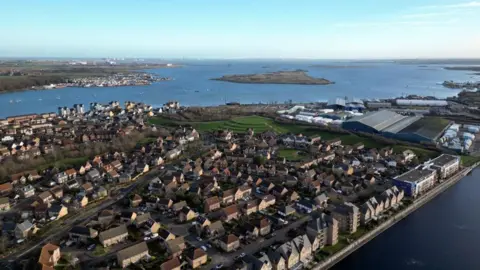 An aerial view of St Mary's Island in Rochester shows rows of residential houses beside waterways, with the River Medway, industrial buildings and small islands visible in the background.