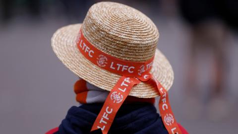 A Luton straw hat with orange football club branding
