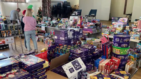 A room with piles of toys and volunteers moving among them