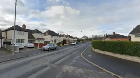 A view of a residential road from a street corner, with white semi-detached houses visible down the road