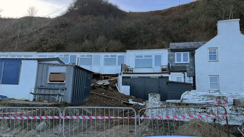 A cordon is placed in front of the properties where a mound of earth and debris has come to rest