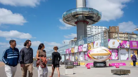 Getty Images Tourists are seen walking on the seafront by the Brighton i360 and the promotion of the Women's Rugby World Cup 2025. Brighton i360 is 162 m (531 ft) moving observation tower on the seafront in Brighton, with a giant rugby ball advertising the women's rugby world cup.