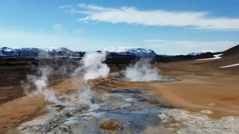 Steam rises from an ice-capped volcanic pool in the distance, northeast in Iceland.