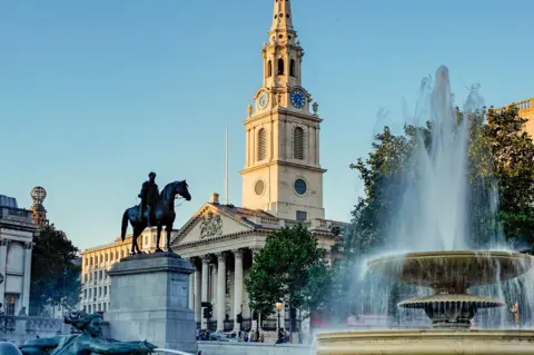St Martin-in-the-Fields The tower and columns of St Martin-in-the-Fields is seen in the sun behind a statue of a man on a horse on a plinth a large fountain in Trafalgar Square