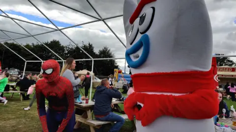 Two people dressed as children's characters are standing in a busy pub garden on a cloudy day.