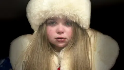 Family photograph 11-year-old Sienna with long brown hair wearing a winter white faux fur hat and matching red velvet and white faux fur collared coat.