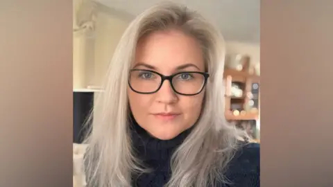 Lyndsay McClay/British Marine A selfie-style image of a woman. She is smiling and has long silver coloured hair. She is wearing glasses and a black turtle neck top.