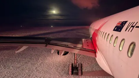 Supplied: Skytraders An aeroplane sits on the snow in the dark with the moon seen through the clouds