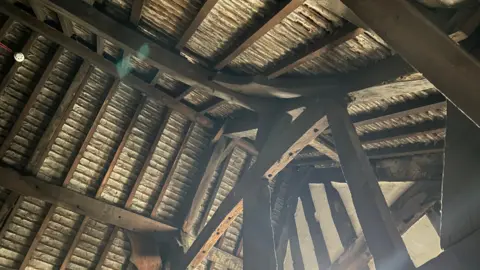 The inside roof of an old mansion building. It is wooden with large dark wood beams, as well as wooden supports.