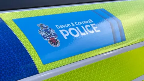 A close up picture of the outside of a police car. It shows the Devon & Cornwall Police logo and the car is wrapped in the usual yellow and blue police colours. 