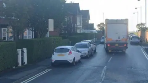 A lorry and parked cars on a sunny day