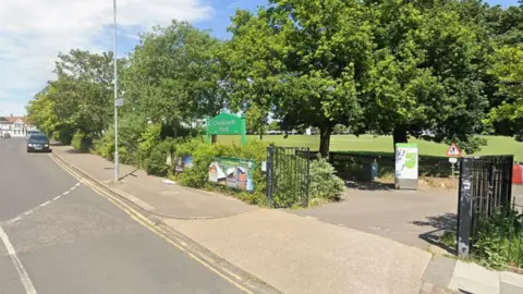 Google The entrance to Chalkwell Park with open black gates and a green sign with the name on. There are lots of mature trees around the edge, and a large lawn behind them.