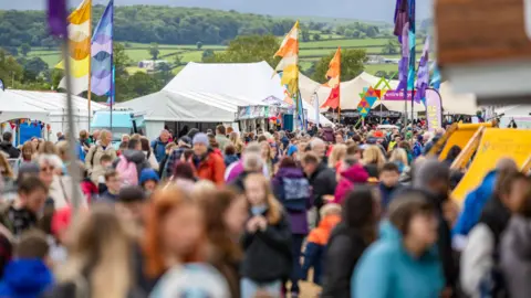 Urdd  A shot of a crowd at a festival with colourful flags and white tents in the background 