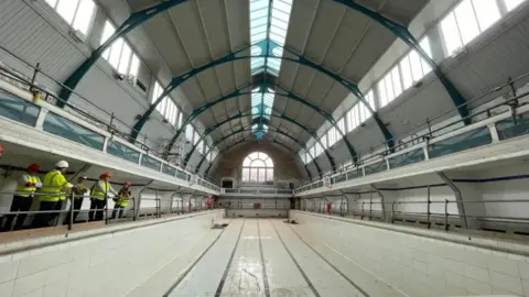 Swindon Borough Council A drained pool with a large rounded roof. To the side of the pool are men in high-vis jackets.