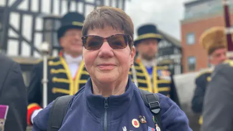Joyce Nicolls is pictured wearing dark glasses and a blue zip up fleece jumper. She has a short brown pixie hairstyle.