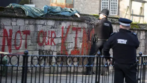 Reuters A police officer pulls a tarp over the words "Not Our King" painted on a wall outside St. Asaph Cathedral.