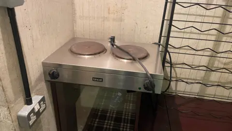 Edd Smith/BBC A retro-style cooker in front of a white concrete wall and next to a plug socket.