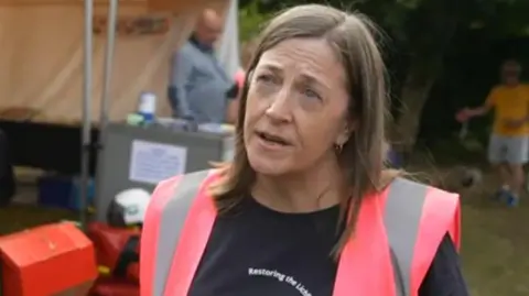 A woman wearing a t-shirt with a slogan saying "restore the Lichfield canal" and a pink hi-vis hacket