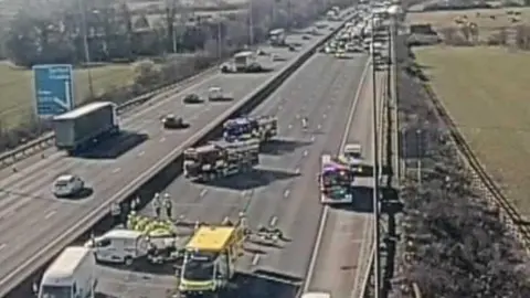 National Highways A traffic camera images shows the closed anticlockwise lane. Traffic is being held and a section of the road is clear while paramedics work at the scene. Fire engines and police are also at the scene. 