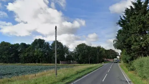 Google Google view of Croft Bank, near Skegness. There are vehicles in the distance and trees and crop fields in view.