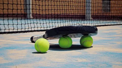 Getty Images A padel racquet and balls on the floor next to a net