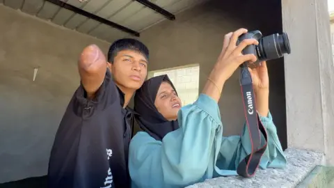 Diya al-Adini and her sister Aya stand shoulder to shoulder as Aya holds up Diya's camera to take a picture