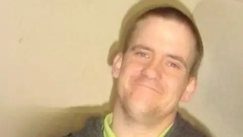 A photo of Dale Stogden, who has shaved dark hair. He is smiling at the camera.