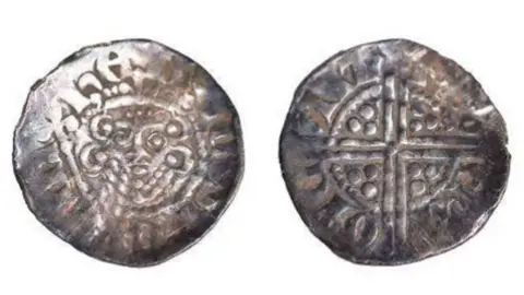 A silver Medieval coin photoaged from the front and back. The coin is shiny with a Celtic cross engraved on one side and a monarch's face on the other.