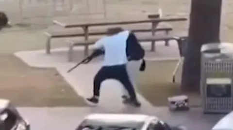 BBC A still image of a man in a white t-shirt tackling a gun from a shooter