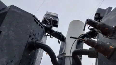 Cambs County Council Part of a traffic light mechanism shows cameras or detector units and cables mounted on a pole.