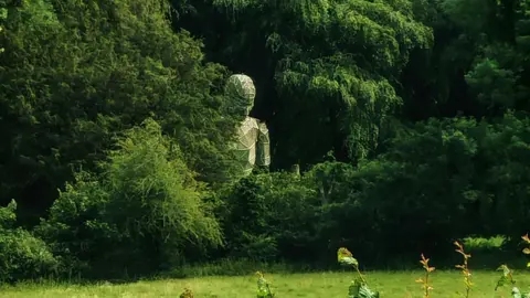 Image of a large robot statue half hidden behind trees in a field