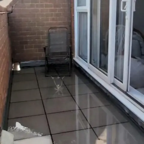 Anna Williams A balcony which has an inch or two of pooling water. A garden chair is in the flooded bit