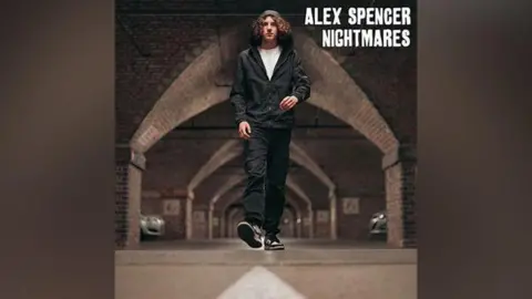 Alex Spencer cover of a single, showing a young man with long curly hair walking through the underground car park in a hooded top with the hood pulled up